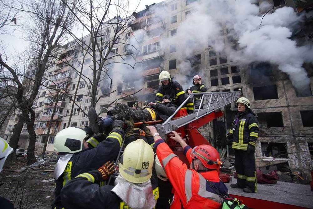 In this handout picture taken and released by the State Emergency Service of Ukraine on March 14, 2022, firemen help a man to evacuate from an apartment building hit by shelling in the Obolon district of Kyiv. AFP PHOTO / State Emergency Service of Ukraine / handout