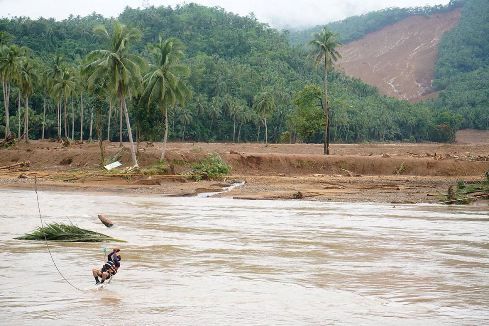 A rescuer crosses a river using a zip line in an attempt to reach the landslide-hit village of Kantagnos in Baybay town, Leyte province on April 13, 2022, following heavy rains brought about by Typhoon “Agaton” (Photo by BOBBIE ALOTA / AFP)