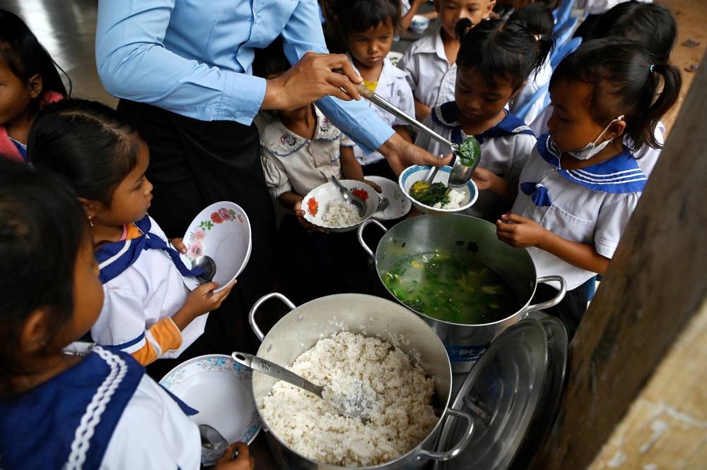 This photo taken on July 8, 2022 shows a teacher serving up breakfast to students before classes with Cambodia's school meals programme at a school in Siem Reap province. - Among the spinach crops at a rural Cambodian school garden, children test their mathematics skills weighing produce -- but as food price rises rock struggling households, the veggie patch has become a critical safety net. (Photo by TANG CHHIN Sothy / AFP) / To go with 'CAMBODIA-HEALTH-EDUCATION,FEATURE' by Suy SE and Lisa MARTIN in Bangkok