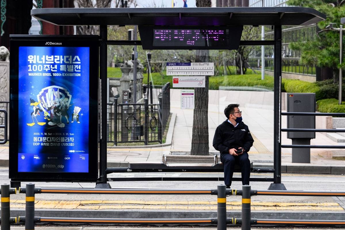 A man sits at a bus stop in Seoul on March 28, 2023, as unionised Seoul Bus drivers went on strike, bringing over 7,200 buses to a full stop and disrupting commute hours in the South Korean capital over a wage hike dispute. (Photo by ANTHONY WALLACE / AFP)