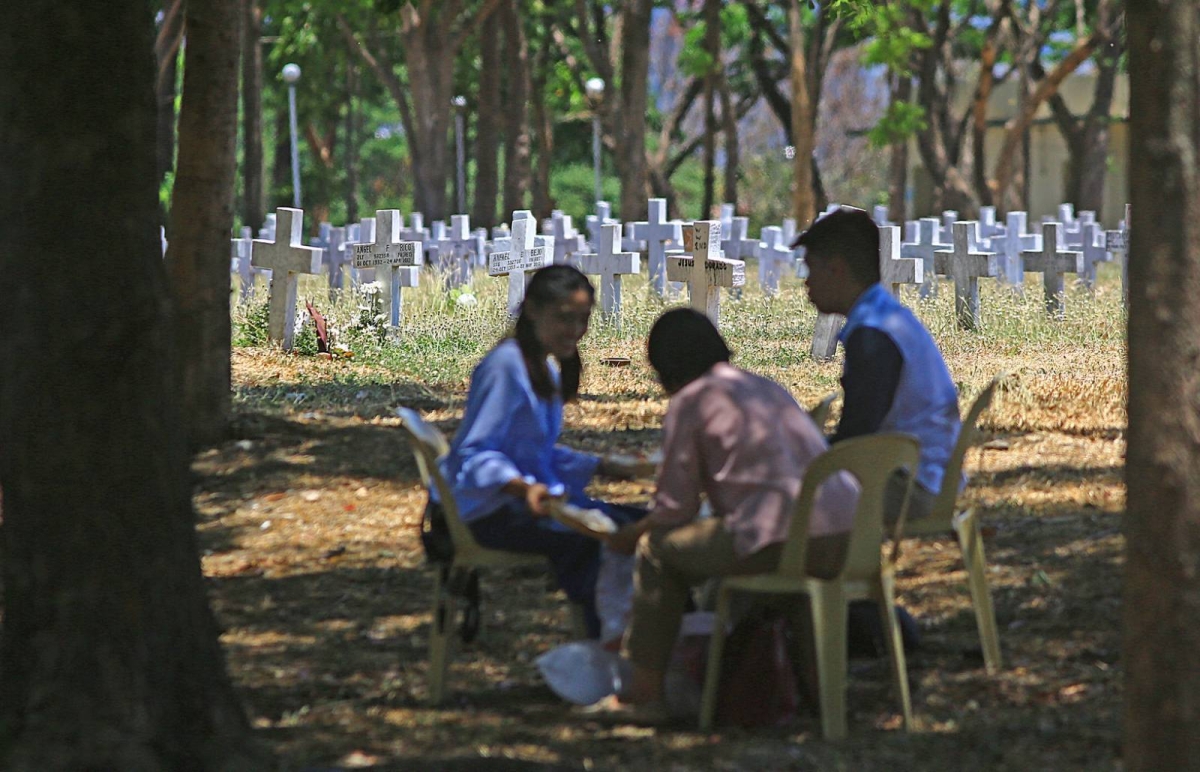 A soldier of the Philippine Army salutes the grave of a fallen soldier and families remember their dead during the Day of Valor or 'Araw ng Kagitingan' inside the Libingan ng mga Bayani (LNMB) in Taguig City, on Tuesday, April 9, 2024. PHOTOS BY MIKE ALQUINTO