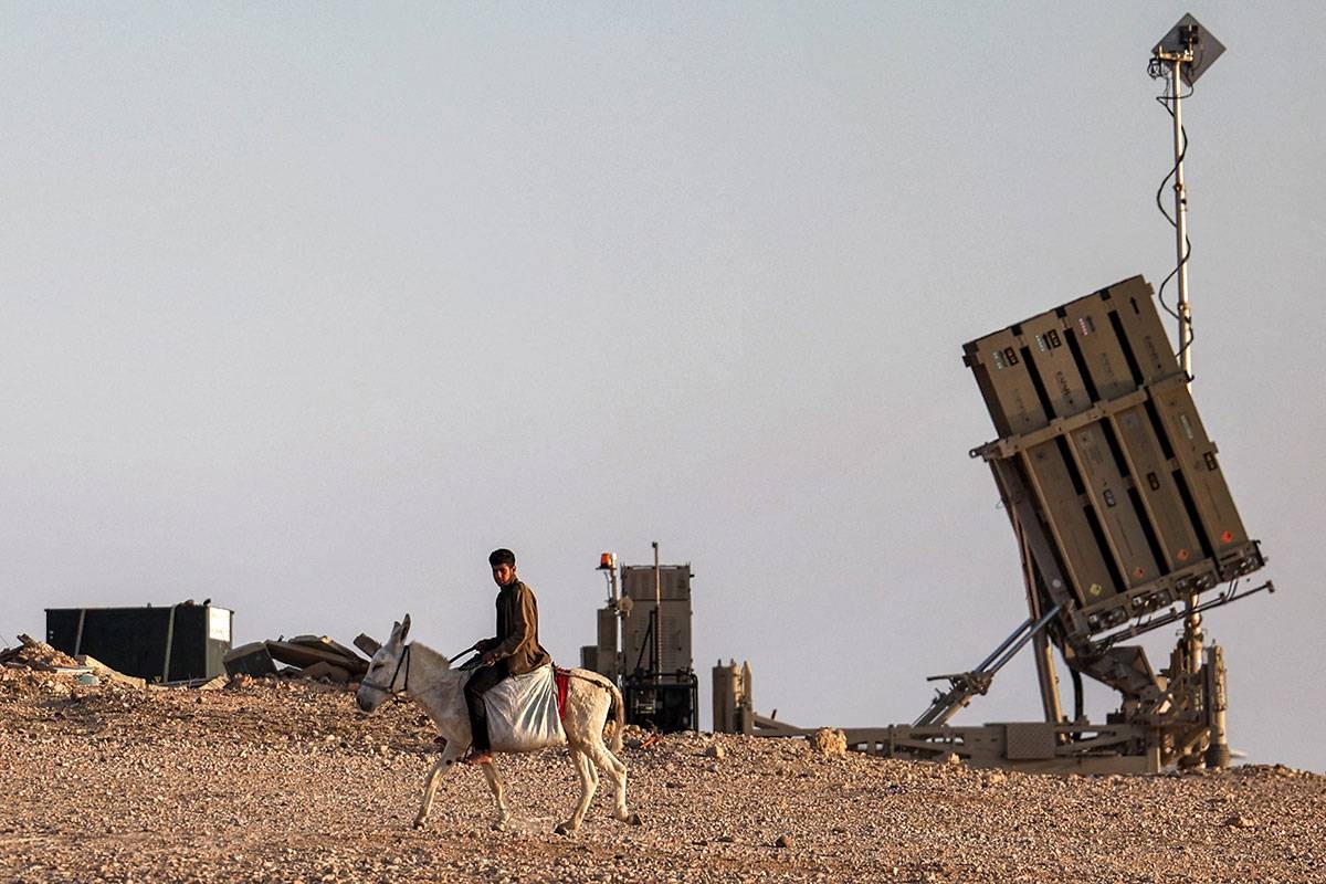 A boy rides a donkey near one of the batteries of Israel's Iron Dome missile defence system at a village not recognised by Israeli authorities in the southern Negev desert on April 14, 2024. AHMAD GHARABLI / AFP