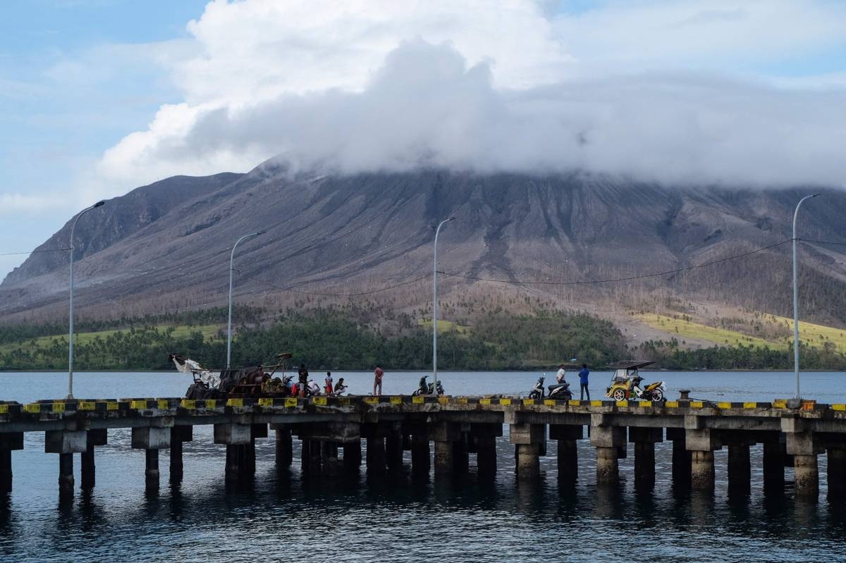 STAYING ALERT People gather on a pier at the port on Tagulandang island in Sitaro, North Sulawesi, on Friday, April 19, 2024, as the Mount Ruang volcano is seen in the background spewing smoke. AFP Photo