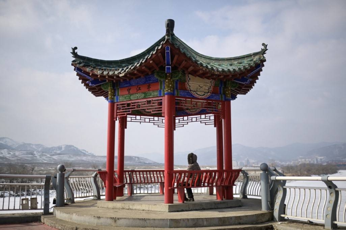 This photo taken on February 29, 2024 shows a woman sitting on a bench, looking at North Korea's Chunggang county, in Linjiang in the province of Jilin, northeast China. AFP PHOTO