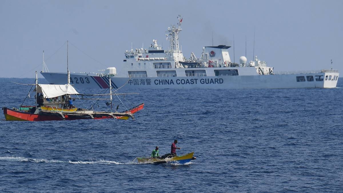 WATCHED A China Coast Guard ship monitors Philippine fishermen aboard their wooden boats during the distribution of fuel and food to fishers by the civilian-led mission Atin Ito (This Is Ours) Coalition in the disputed South China Sea on May 16, 2024. A Philippine boat convoy bearing supplies for Filipino fishers said they were headed back to port May 16, ditching plans to sail to a Beijing-held reef off the Southeast Asian country after one of their boats was ‘constantly shadowed’ by a Chinese vessel. Photo by Ted ALJIBE/AFP