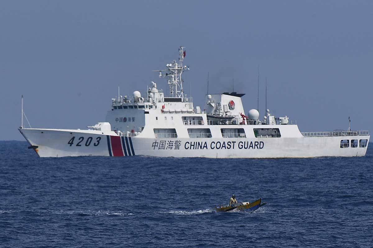 A China Coast Guard ship monitors a Philippine fisherman aboard his wooden boat during the distribution of fuel and food to fishers by the civilian-led mission Atin Ito (This Is Ours) Coalition, in the disputed South China Sea on May 16, 2024. A Philippine boat convoy bearing supplies for Filipino fishers said they were headed back to port May 16, ditching plans to sail to a Beijing-held reef off the Southeast Asian country after one of their boats was "constantly shadowed" by a Chinese vessel. Ted ALJIBE / AFP