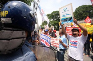 A policemen watches as members of militant groups hold a rally in front of the offices of the Manila Waterworks and Sewerage System (MWSS) in Quezon City on Friday. The groups lambasted the agency for allowing water concessionaires to pass on their taxes to consumers. Photo By Miguel De Guzman