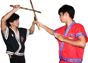 The attacker delivers an overhead strike with cane. Punong Lakan Garitony Nicolas (left) blocks the strike using an upper X block with his cane [representing the sword] and his dagger.