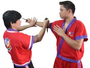 The attacker delivers a high stab with his right hand. Punong Lakan Garitony Nicolas checks the attacker’s knife hand with his left hand while performing an upward cut on the elbow crook with his knife.