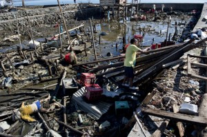 A man starts to rebuild his house as the body of a victim lies among debris in a Tacloban neighborhood.  AFP PHOTOS  