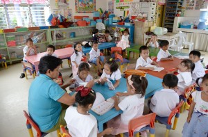 In Ibabao, children listen to their teacher at a day care center next to the now abandoned house (back) that used to stream live sex acts of children to pedophiles watching online overseas. AFP PHOTO