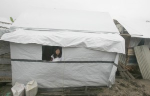 A woman looks out from the window of her temporary shelter in Tacloban City. One hundred days after Yolanda struck, millions remain without adequate shelter. PHOTO BY RENE H. DILAN