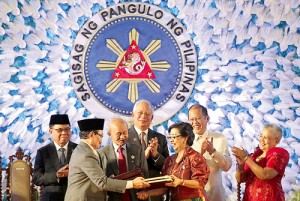 MILF chief negotiator Mohagher Iqbal (left) exchanges copies of the agreement with his government counterpart, Miriam Coronel-Ferrer, as MILF Chairman Al Haj Murad Ibrahim, Peace Facilitator Tengku Dato Abdul Ghafar Tenku Mohammed, Malaysian Prime Minister Najib Razak, President Benigno Aquino 3rd and Presidential Adviser on the Peace Process Secretary Teresita Quintos-Deles applaud. MALACAÑANG PHOTO