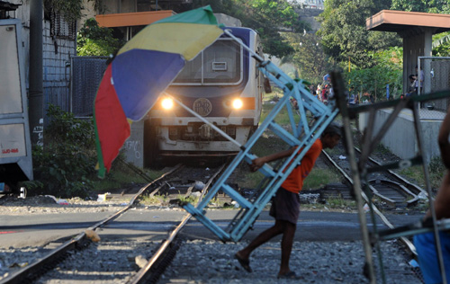 A man lifts his makeshift trolley off the rails to allow a train to pass through in Manila. Small-time entrepreneurs push commuters on their trolleys, charging a small fee for transporting them short distances. AFP PHOTO 