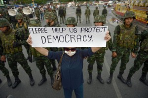 An anti-coup protester holds up a sign past soldiers as she takes part in a rally at Victory Monument in Bangkok on Monday. AFP PHOTO