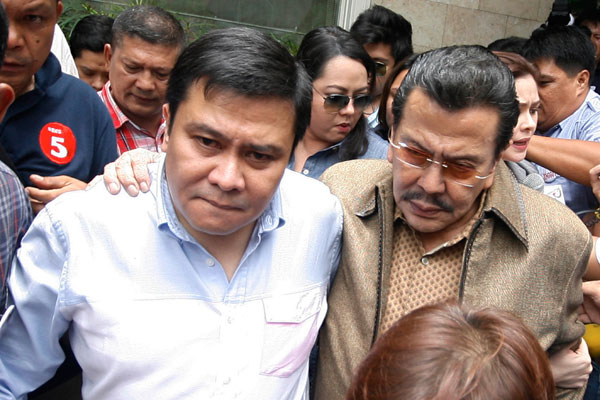 Former President Joseph Estrada stays close to his son, Sen. Jose “Jinggoy” Estrada, as they arrive at PNP headquarters in Camp Crame on Monday.  Photo By Miguel De Guzman 