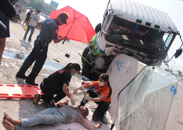 An emergency responder attends to a gas delivery helper who was thrown out of his truck when it hit a creek barrier in Quezon City. The driver, who was also injured, said the brakes failed. PHOTO BY RUY MARTINEZ