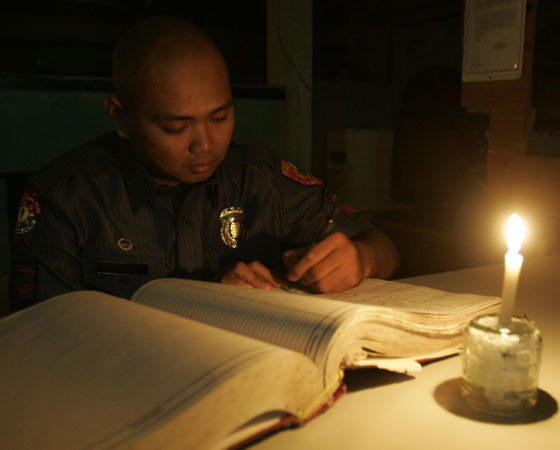 With just a candle for light, homicide investigator Rommel del Rosario writes in a blotter at the Manila Police District headquarters on Saturday. The MPD was one of areas hit by rotating brownouts caused by power supply deficiency.  PHOTO BY RENE H. DILAN 