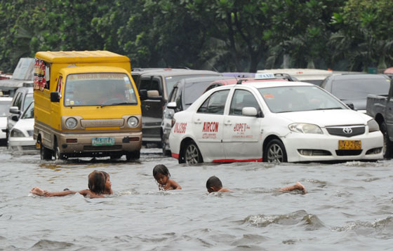 Children play in a street submerged by heavy rains overnight while motorists drive past in Manila on Tuesday.  The weather bureau issued a yellow rain warning in city on the same day due to a low pressure area in the Bicol region, southeast of Manila. AFP Photo