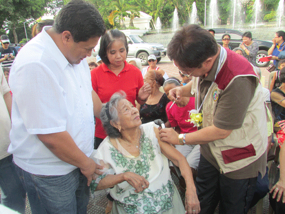 Mimaropa (Mindoro, Marinduque, Romblon and Palawan) Regional Director Eduardo Janairo (right), assisted by Pinamalayan Vice Mayor Aristeo Baldos Jr., gives a pneumococcal vaccination to a 93-year-old Primitiva Lamboloto in line with the Department of Health’s immunization program. CONTRIBUTED PHOTO