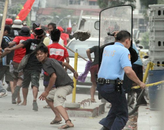 A policeman takes cover as a man throws a stone during a protest rally near the residence of President Benigno Aquino 3rd in Times Street in Quezon City. The dispersal of the rallyists turned violent when some protesters started hurling stones, paint and other hard objects at policemen. PHOTO BY MIKE DE JUAN