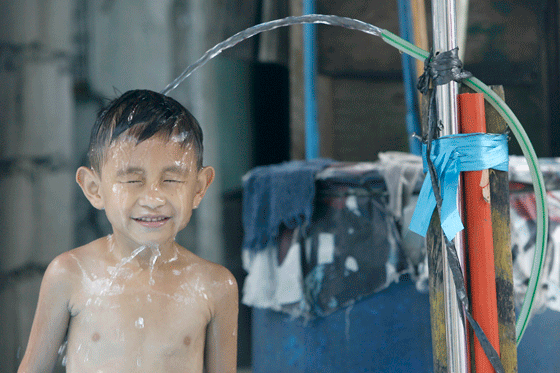 A boy cools off under running water from a hose as he and his friends set up an inflatable pool along a street in Quezon City to beat the intense heat of summer on Sunday. PHOTO BY MIGUEL DE GUZMAN