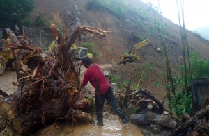 GO AHEAD, MAKE MY WAY  A worker cuts up a fallen tree while heavy equipment (in background) works to clear debris and soil after a mountainside eroded due to heavy rains brought about by typhoon Ineng, along Kennon road, a main road leading to Baguio City on Saturday.  AFP PhOTO 