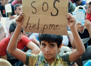 OUT-OF-CONTROL HUMAN TRAGEDY  A migrant boy holds a sign reading ‘SOS help me’ as he sits with other migrants in front of the Keleti (East) railway station in Budapest on September 2. Heartbreaking images of another child, his lifeless body washed up on a Turkish beach, have provoked widespread anger at the apparent inability of the EU to cope with the largest movement of refugees since WWII. AFP PHOT