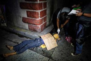EXECUTED In this picture taken on July 8, 2016, police officers inpect the dead body of an alleged drug dealer, his face covered with packing tape and a placard reading “I’m a pusher”, on a street in Manila. AFP PHOTO