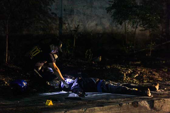 A crime investigator examines the dead body of one of two motorcycle-riding individuals killed following a shootout with police on C-3 Road in Caloocan on August 28. PHOTO BY DJ DIOSINA