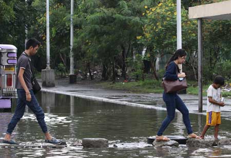  Commuters cross a makeshift footpath along P. Burgos Avenue in Manila on Sunday to stay clear of the road that had been flooded by heavy rains. PHOTO BY RUSSELL PALMA