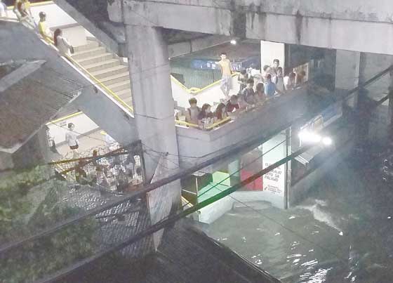 Commuters wait for floodwaters to subside at the Light Rail Transit station on R. Papa Street in Manila, after heavy rains on Saturday. PHOTO BY LANZ MENDOZA