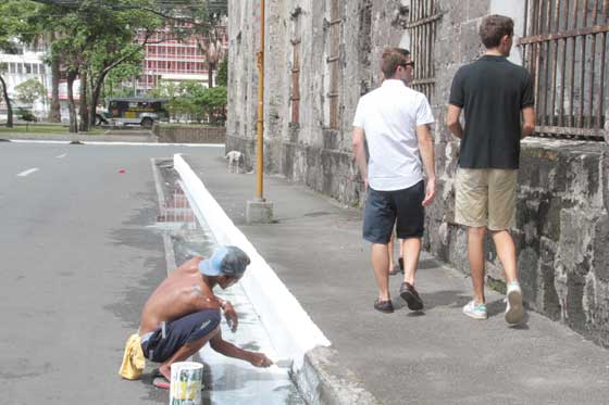 A worker paints part of a sidewalk as two foreign tourists walk past him on Aduana Street in Intramuros, Manila, on Sunday. Intramuros or the Walled City is a top tourist draw but it apparently has helped little in putting the Philippines atop the list of favorite destinations of foreigners. As of May 2015, according to the World Economic Forum, the Philippines ranked 74 among 141 countries most visited by international travelers. PHOTO BY ROGER RAÑADA