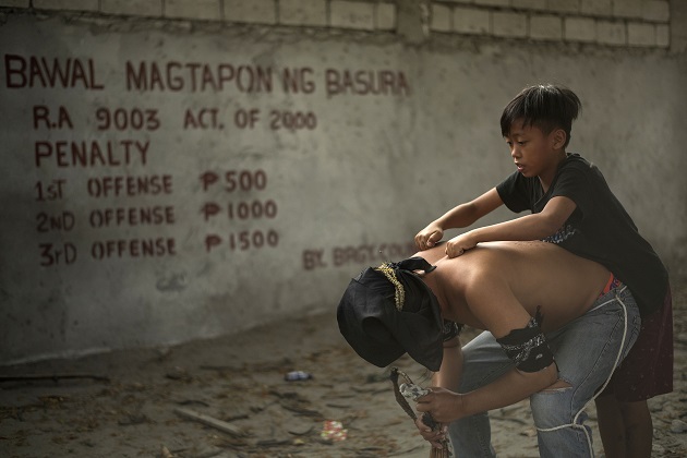 Flagellant Jay Villafuerta has his back massaged by a boy before being wounded as part of his penitence during the re-enactment of the crucifixion of Jesus Christ  in  San Juan, Pampanga,  on March 30, 2018.

